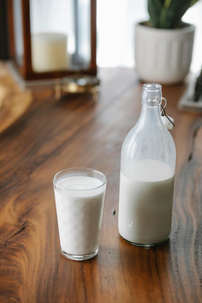 Ornamental glass near transparent bottle of creamy milk on table at home in daylight